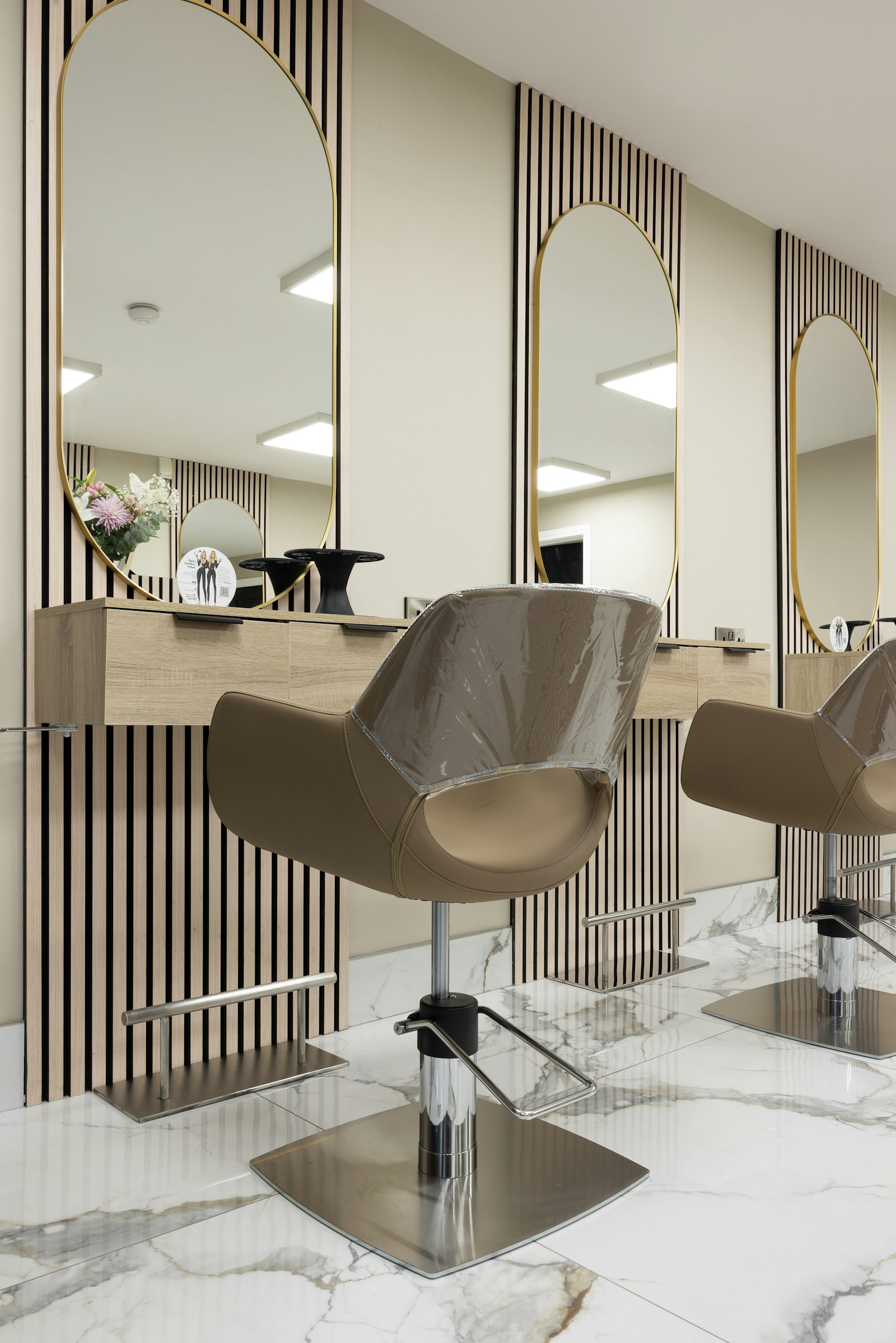 The interior of a modern hair salon with styling chairs, arched mirrors and a marble floor