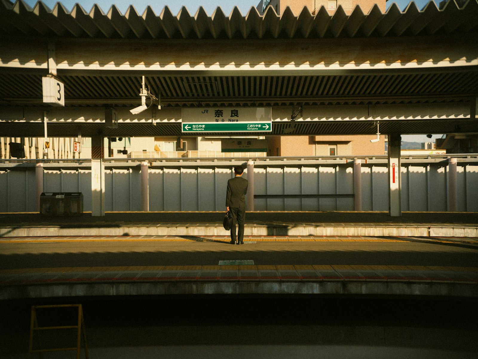 A lone traveler with a bag standing on a JR train platform in Japan at golden hour