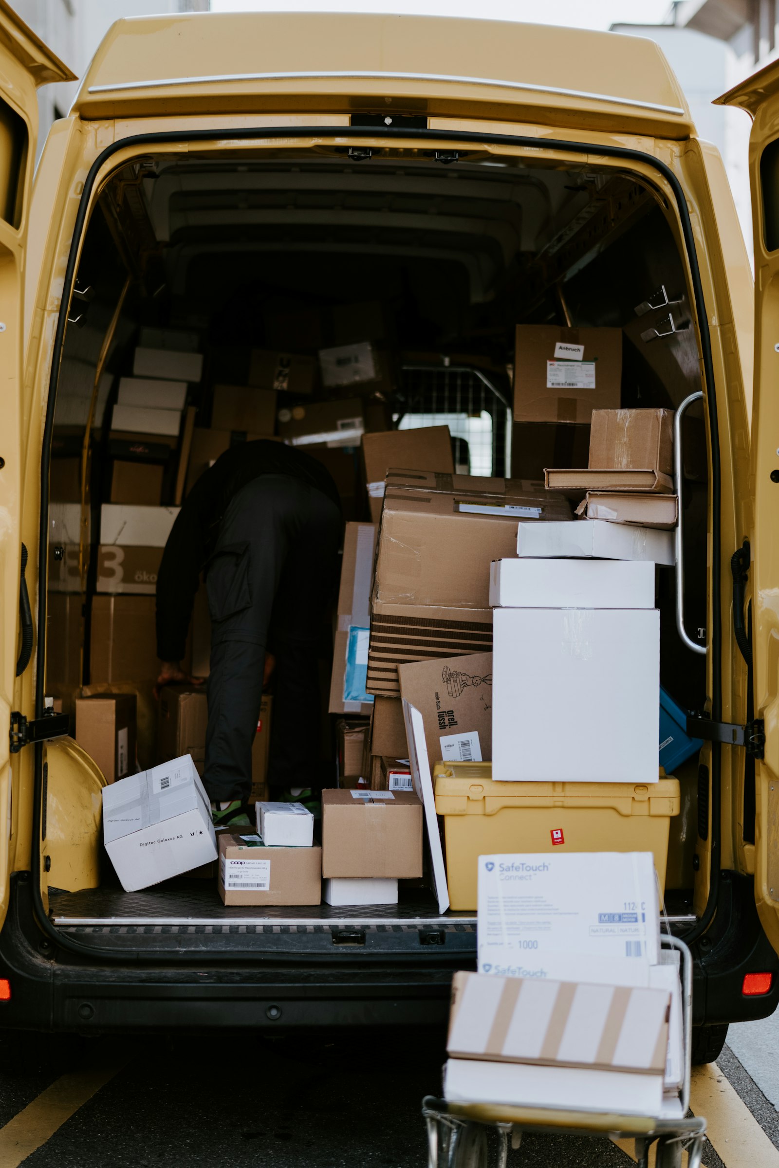 The open back of a delivery van loaded with parcels, a courier sorting them